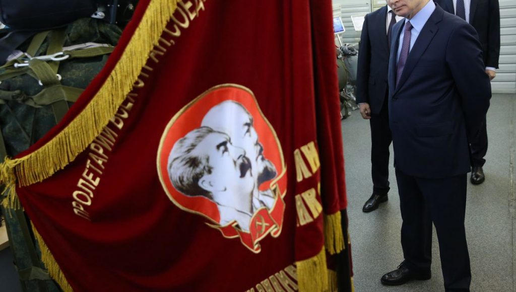Vladimir Poutine devant un drapeau avec Lénine et Staline représentés dessus